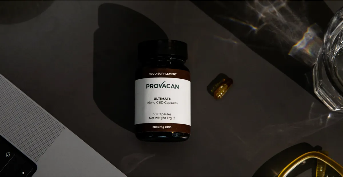 Provacan Ultimate 96mg CBD capsules supplement bottle on a desk next to a glass of water