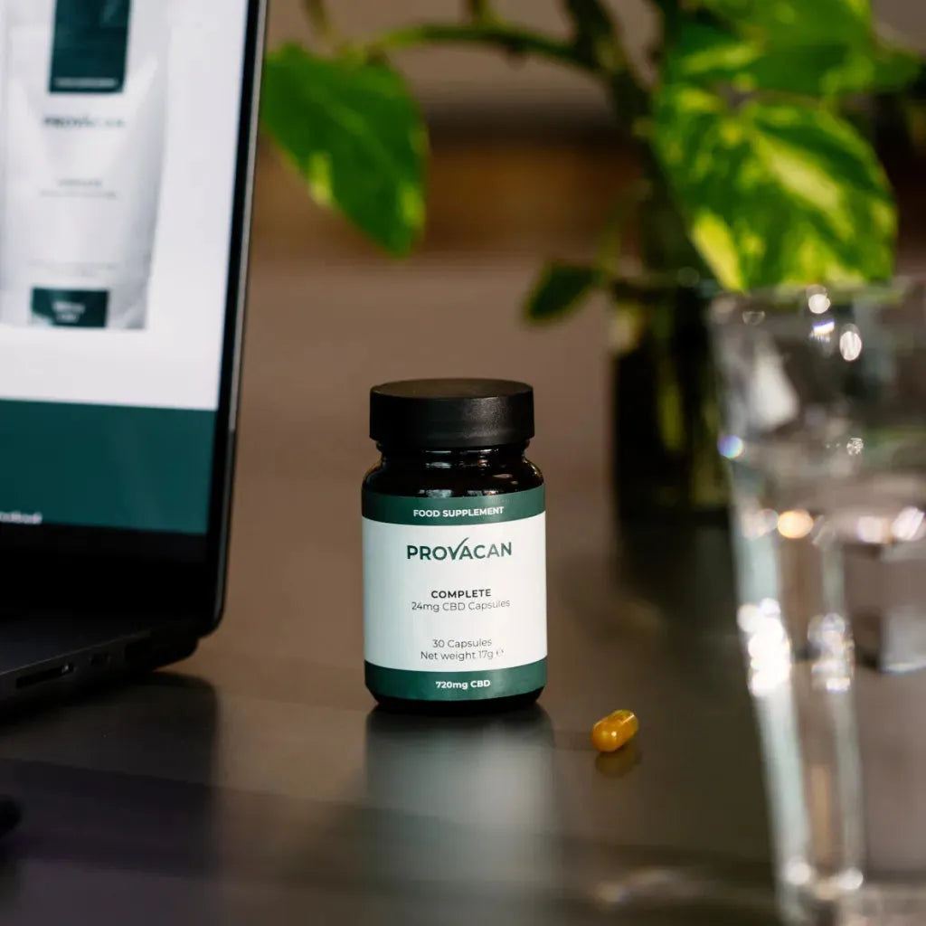 A jar of Provacan Complete 24mg CBD Capsules on a desk next to a work laptop.