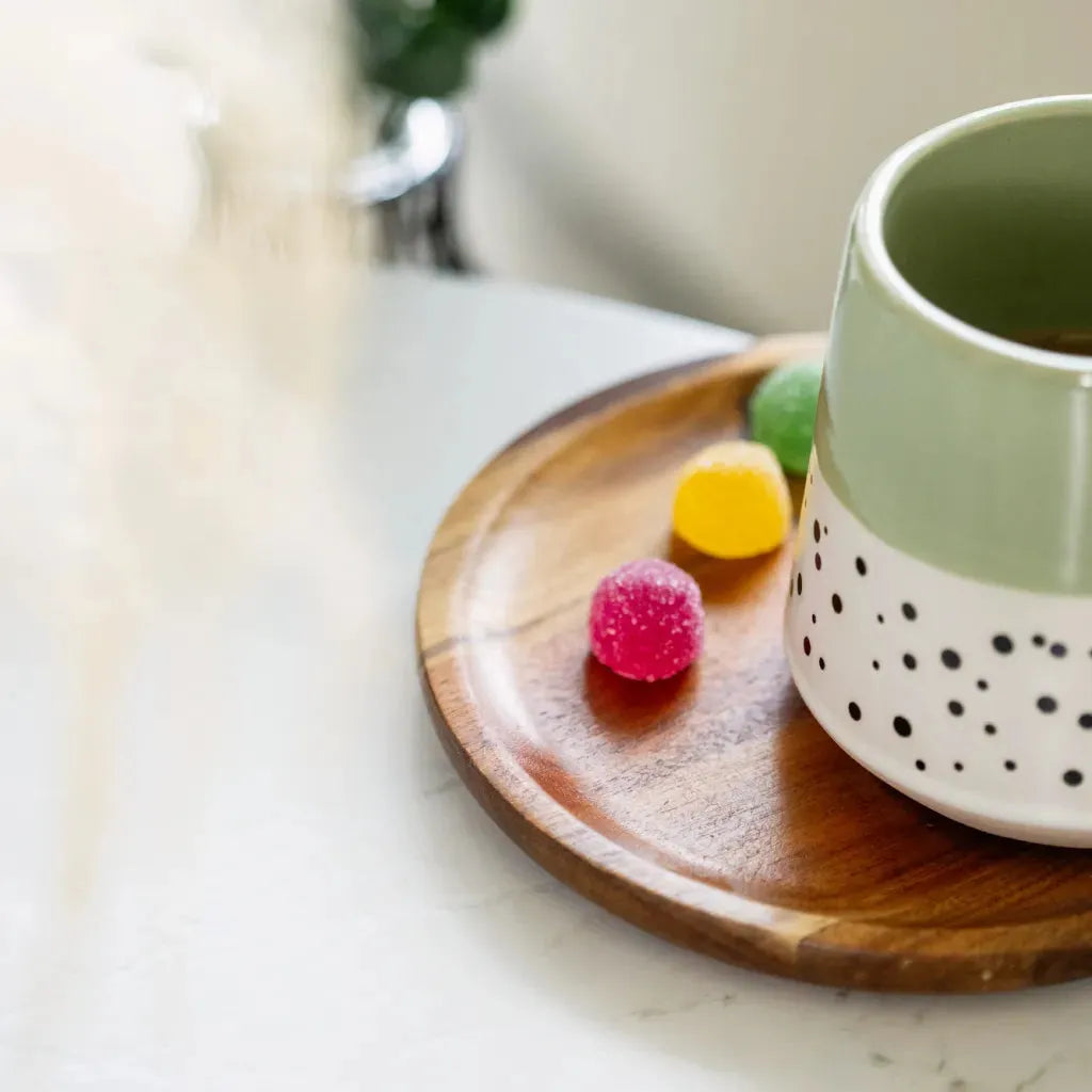 Colourful CBD gummies on a tray next to a coffee mug.