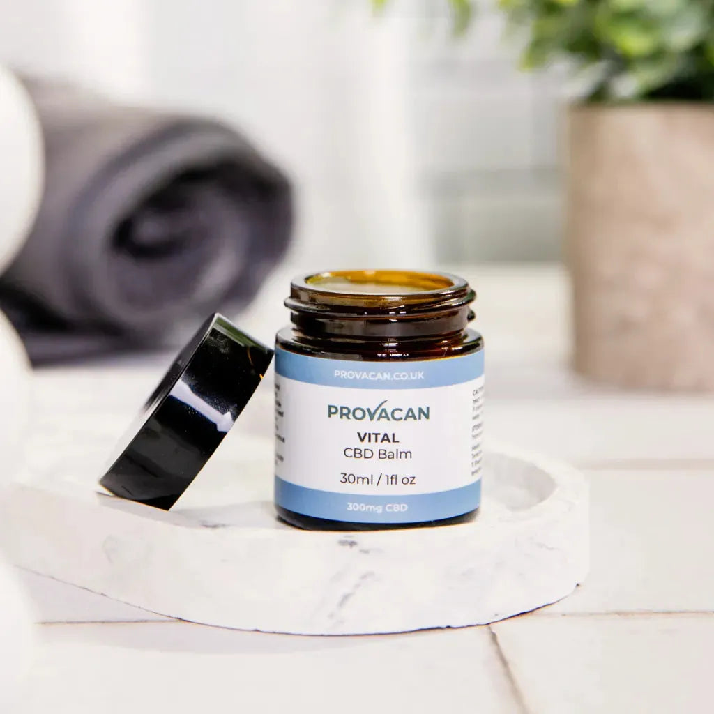An open jar of Provacan Vital CBD Balm on a marble tray in a bathroom.