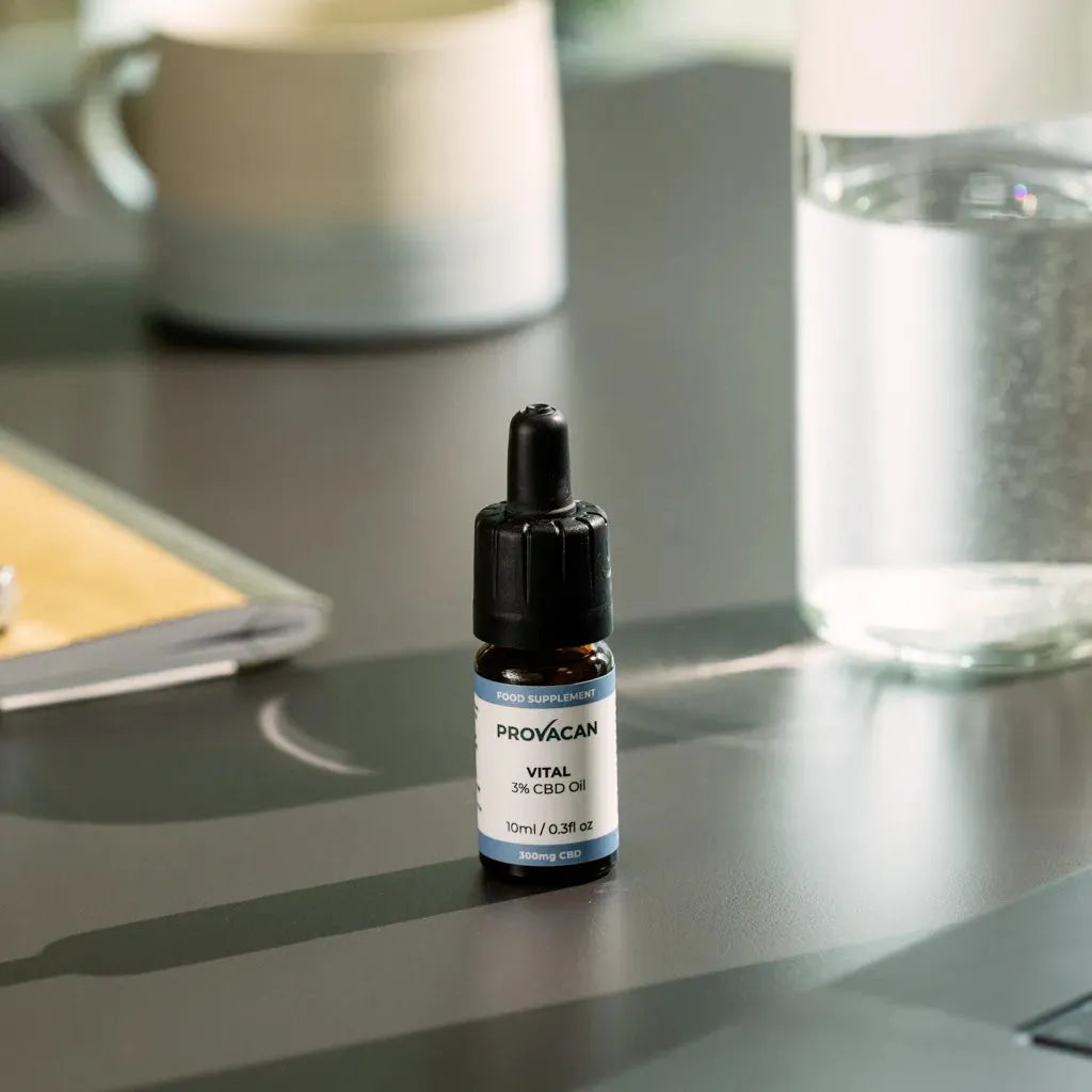 Bottle of Provacan Vital 3% CBD Oil on a desk next to a glass of water