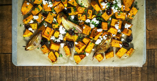 Roasted sweet potato, feta and vegetable dish on a baking tray on top of a wooden table