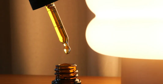 Close-up of a dropper with CBD oil being dispensed into a bottle, with a blurred light source in the background