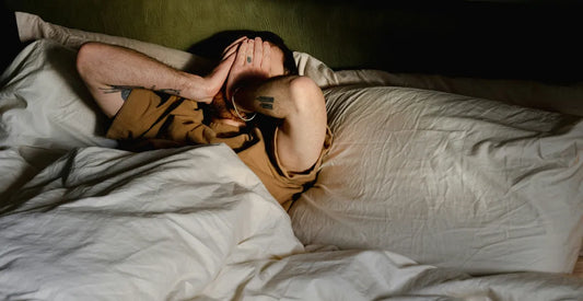 Man lying in bed, covering his face with his hands