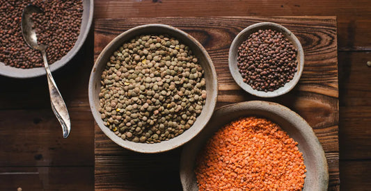 Bowls of green, brown and red lentils on a rustic wooden table, with a spoon