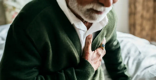 Man in a green sweater holding his chest, possibly indicating heart problems, discomfort or distress
