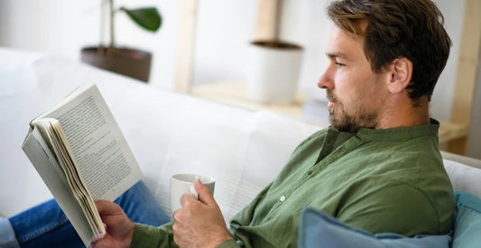 Man reading a book and holding a mug on a couch in a cosy living room