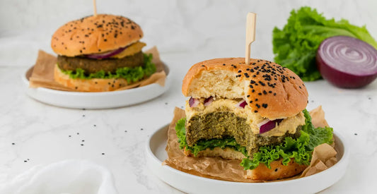 Two plant-based protein vegan burgers on plates on a table with one bite taken out of the front one