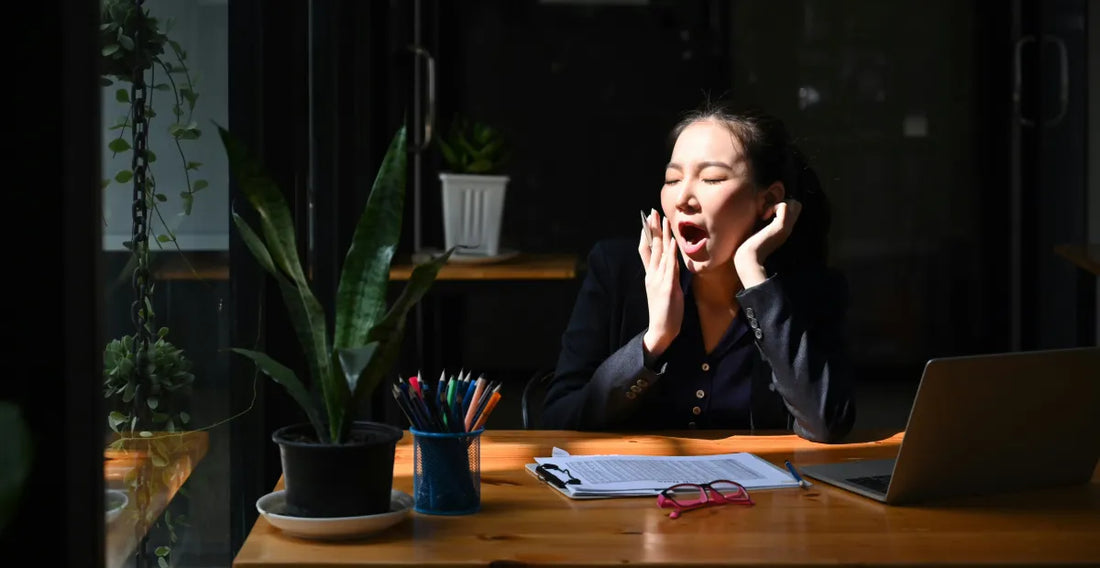 Person sitting at a desk with a laptop, yawning in a dimly lit room
