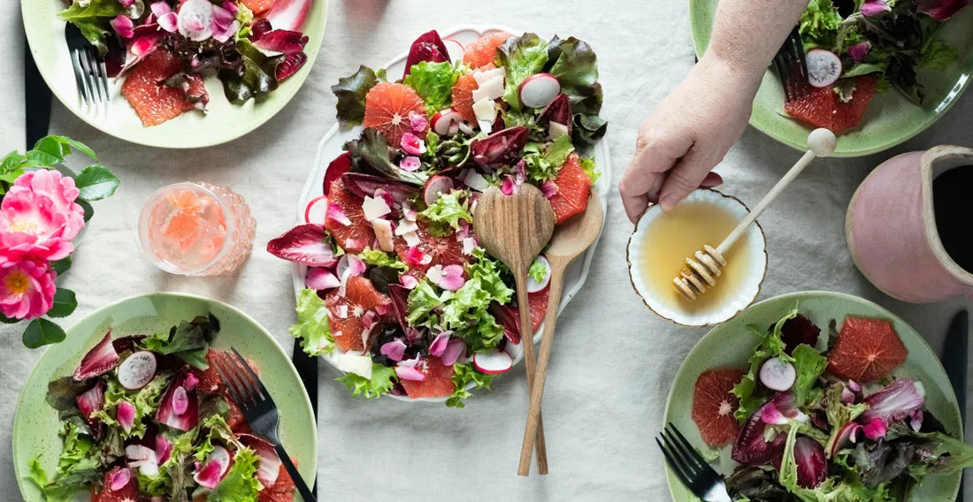 Plates of salad with various ingredients on a table, with a hand holding a small bowl of dressing