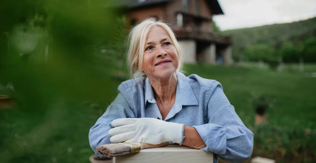 Woman in a blue shirt with white gloves and a paintbrush outdoors in a greenery background