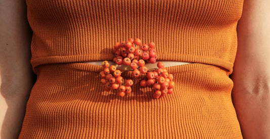 Close-up of a person wearing an orange ribbed outfit with a cluster of berries tucked in clothes on the stomach