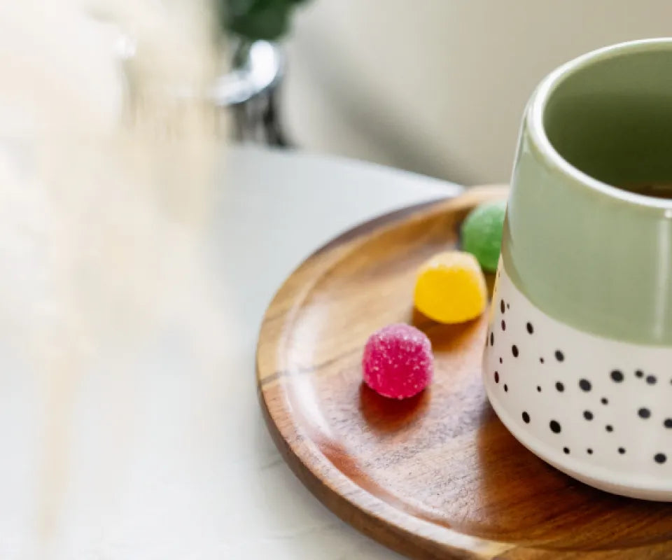 Three colourful Provacan CBD gummies resting on a round wooden tray next to a decorative ceramic mug