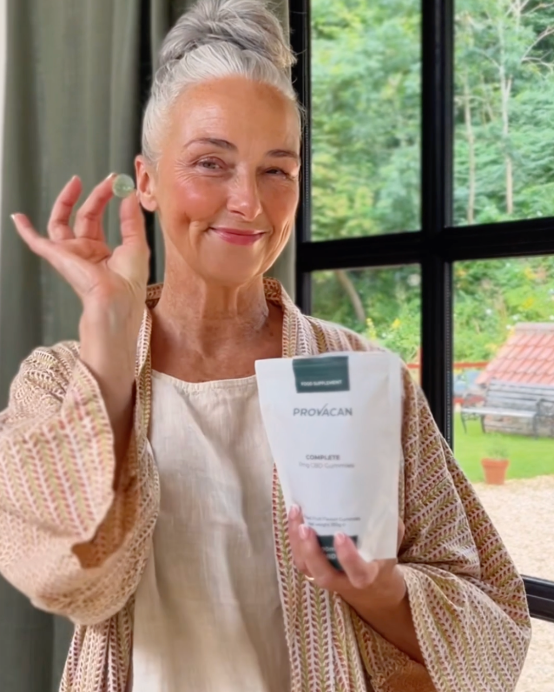 Woman holding a bag of Provacan 10mg CBD Gummies indoors with greenery outside