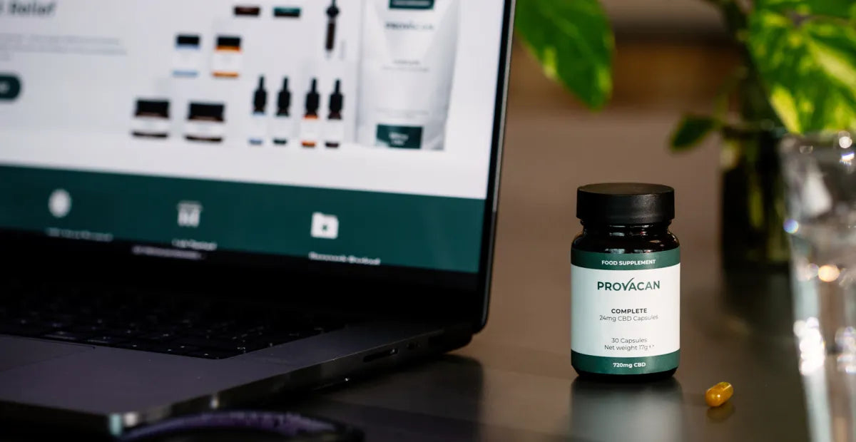 Laptop displaying Provacan's website on a desk next to a bottle of Provacan Complete 24mg CBD capsules
