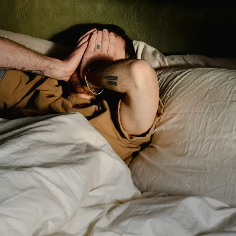Man lying in bed, covering his face with his hands