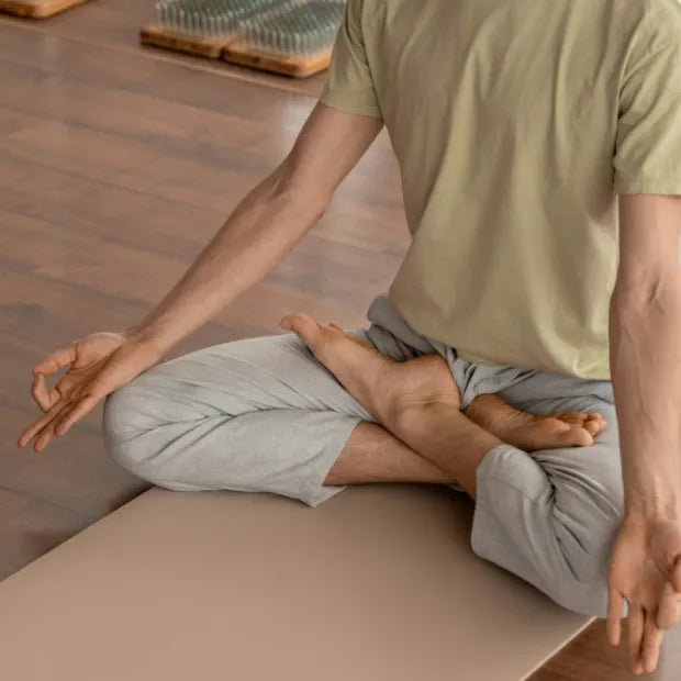 Man sitting on a yoga mat with crossed down and hands on kneecaps, meditating