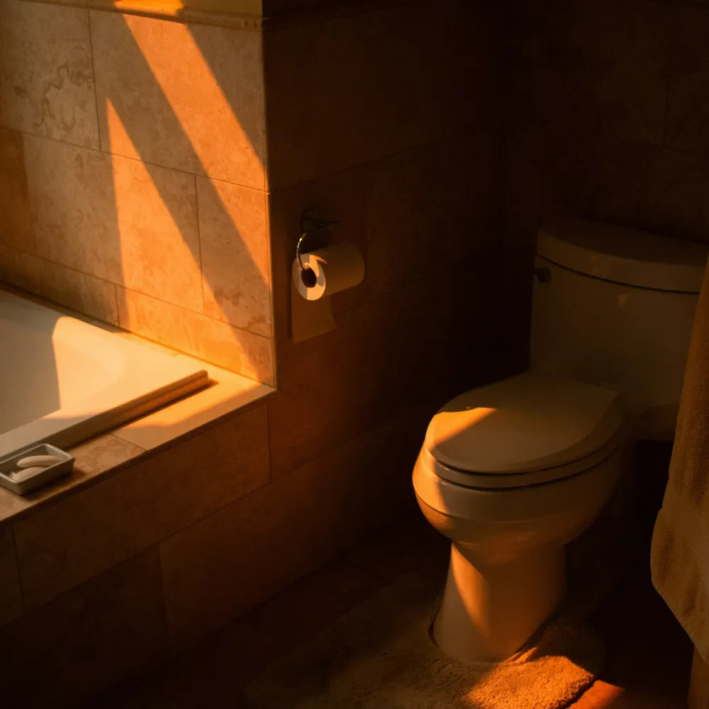 Bathroom scene with a toilet and tiled wall, illuminated by warm light