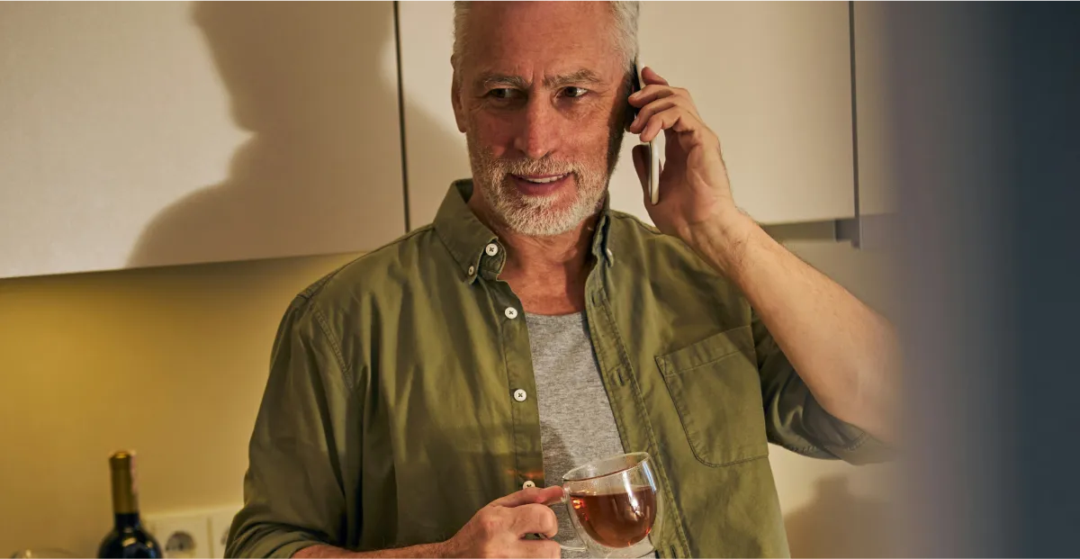 Man in a kitchen holding a cup of tea and talking on the phone
