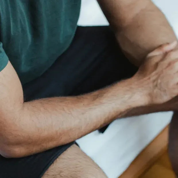 Close-up of man sitting on a bed holding his arm