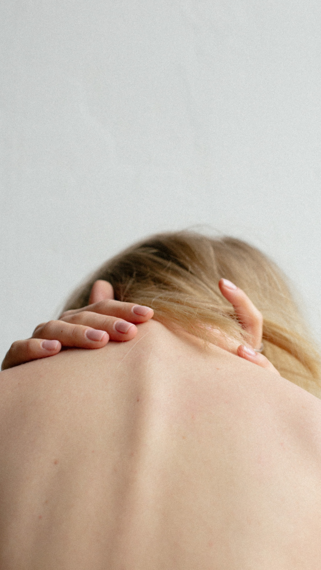 Close-up of a woman's back as she holds her neck