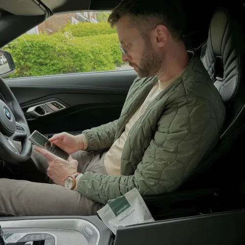 Man sitting in his card on his phone and having a pack of Provacan CBD Gummies next to him