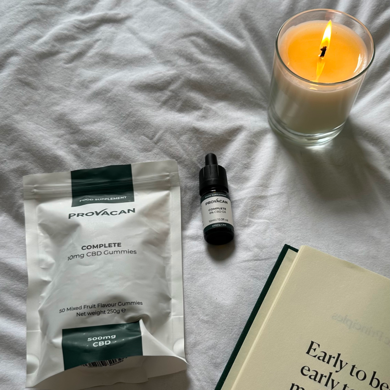 Provacan Complete CBD Gummies 10mg with Provacan Complete CBD Oil 6% 600mg on a bed next to a book and candle