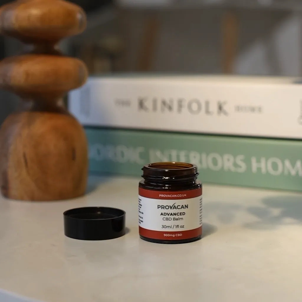 An open jar of Provacan Advanced CBD Balm with home decor in the background. 