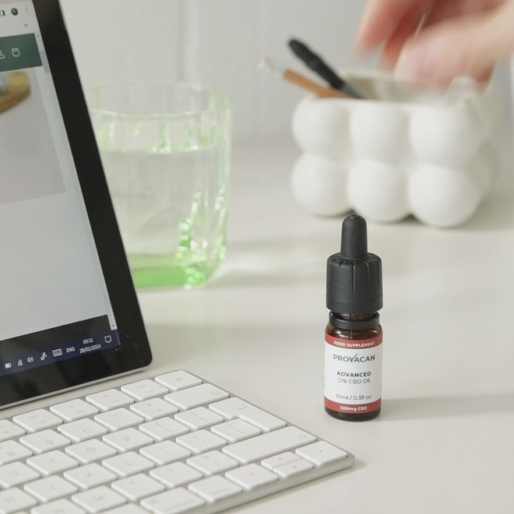 Shot pans across a desk with a laptop, glass of water and Provacan Advanced CBD Oil. Second shot shows a close-up of the Advanced CBD Oil on a concrete block with soft background. 