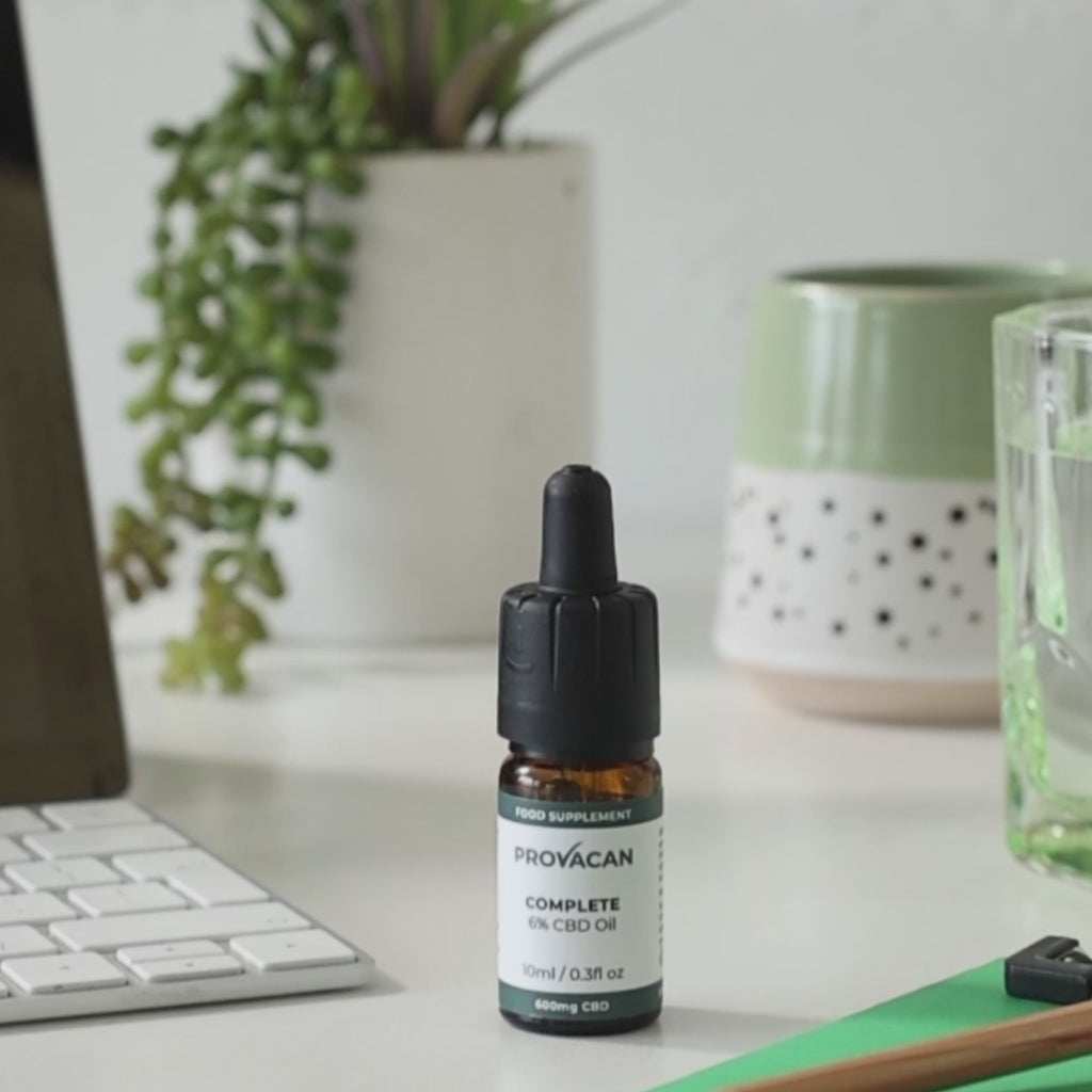 A shot of Provacan Complete CBD Oil on a desk next to a tablet, glass of water, greenery and stationary. A close-up of the same scene with a person lifting the dropper and a few drops of CBD oil being released back into the bottle. 